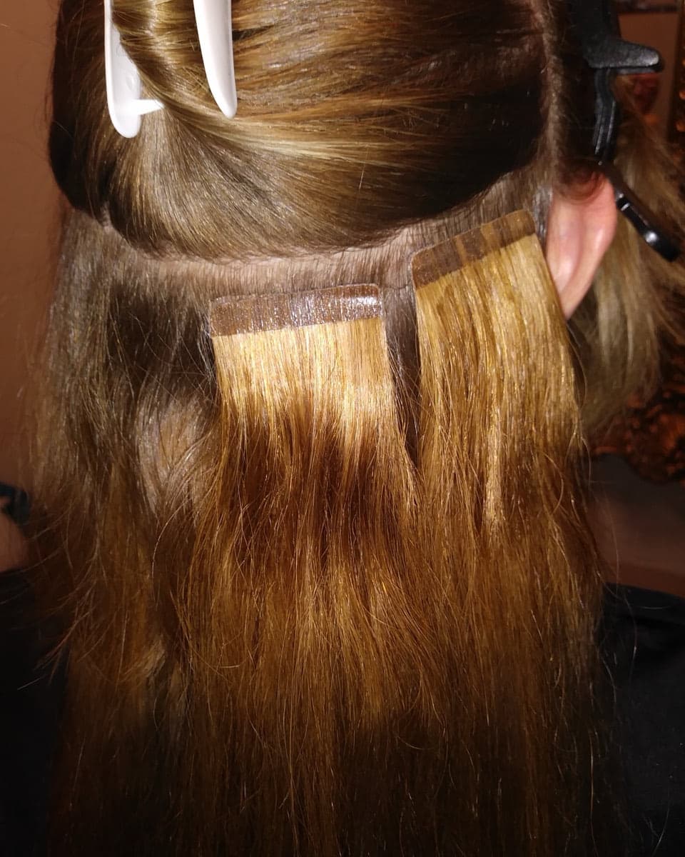 Close-up of tape-in extension wefts applied to sectioned brown hair